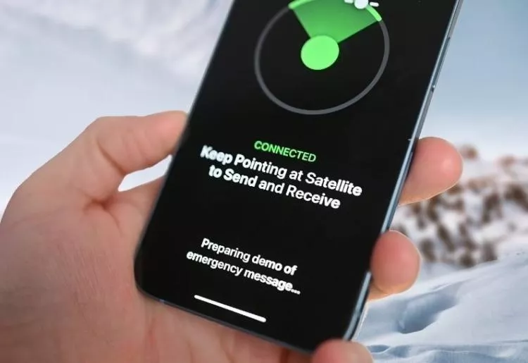 Seseorang memegang iPhone dengan pesan "Connected" ke satelit di lingkungan bersalju, menunjukkan keandalan perangkat Apple.
