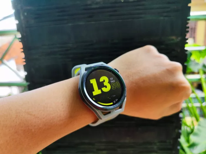 Tampilan smartwatch Huawei yang sedang digunakan di pergelangan tangan menunjukkan angka jam 13:50 dengan watch face berwarna kuning.