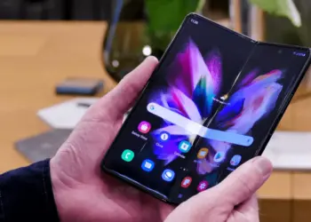 Seorang wanita menggunakan smartphone model terbaru 2026 untuk mengabadikan momen di depan dekorasi lampu.