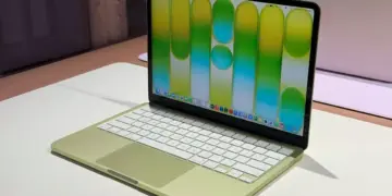 Tampilan layar jernih MacBook Neo berwarna hijau muda yang sedang menyala di atas meja putih, menunjukkan desain elegan dengan bezel tipis.