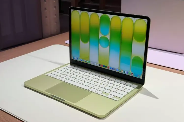 Tampilan layar jernih MacBook Neo berwarna hijau muda yang sedang menyala di atas meja putih, menunjukkan desain elegan dengan bezel tipis.