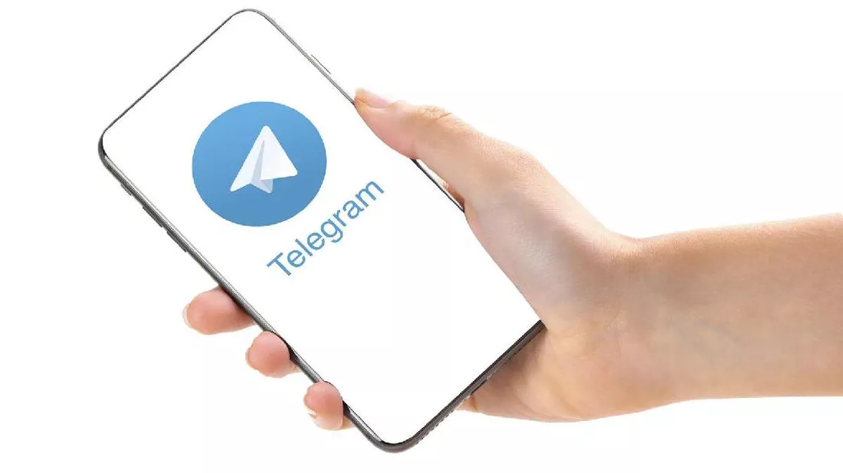 Seseorang memegang smartphone menampilkan logo Telegram pada latar belakang putih bersih.