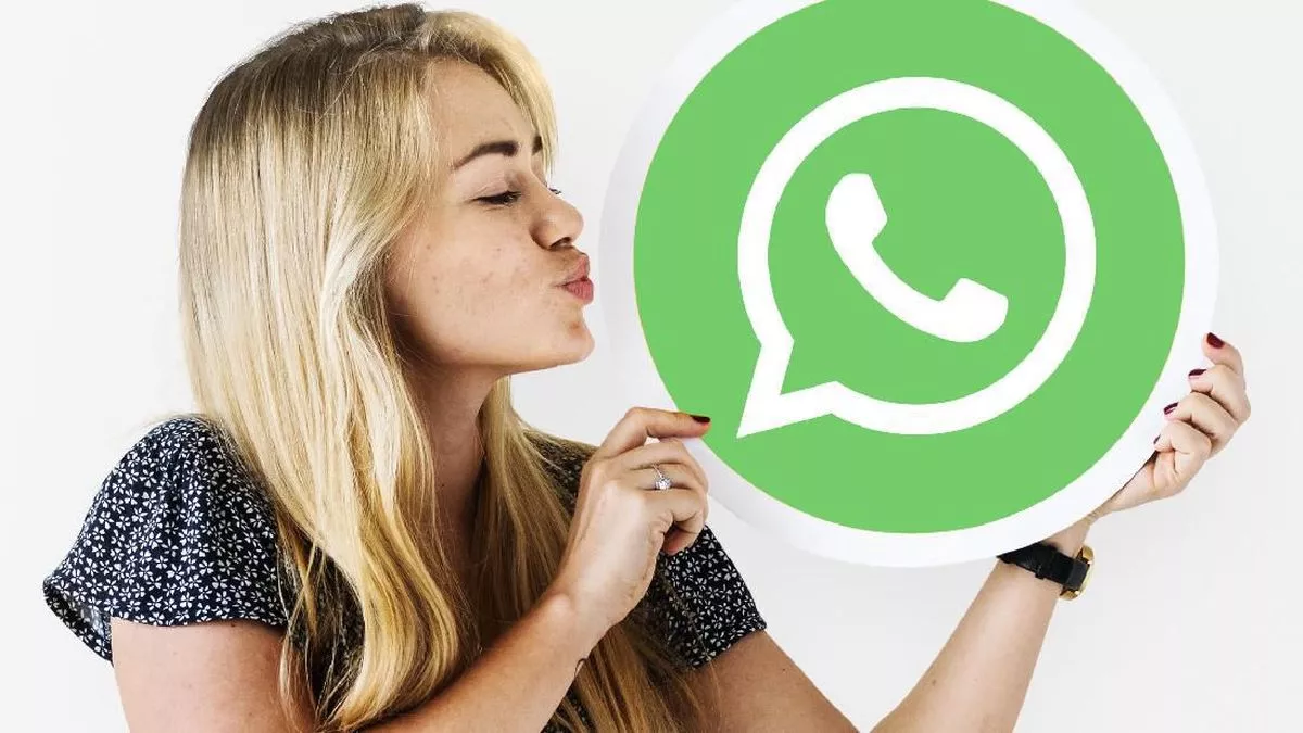 Seorang wanita sedang berpose mencium logo WhatsApp berukuran besar, menunjukkan ekspresi senang menggunakan aplikasi.