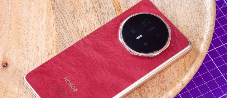 Detail tekstur bodi belakang Honor Magic V6 warna merah di atas meja kayu, menonjolkan modul kamera AI Image yang canggih.