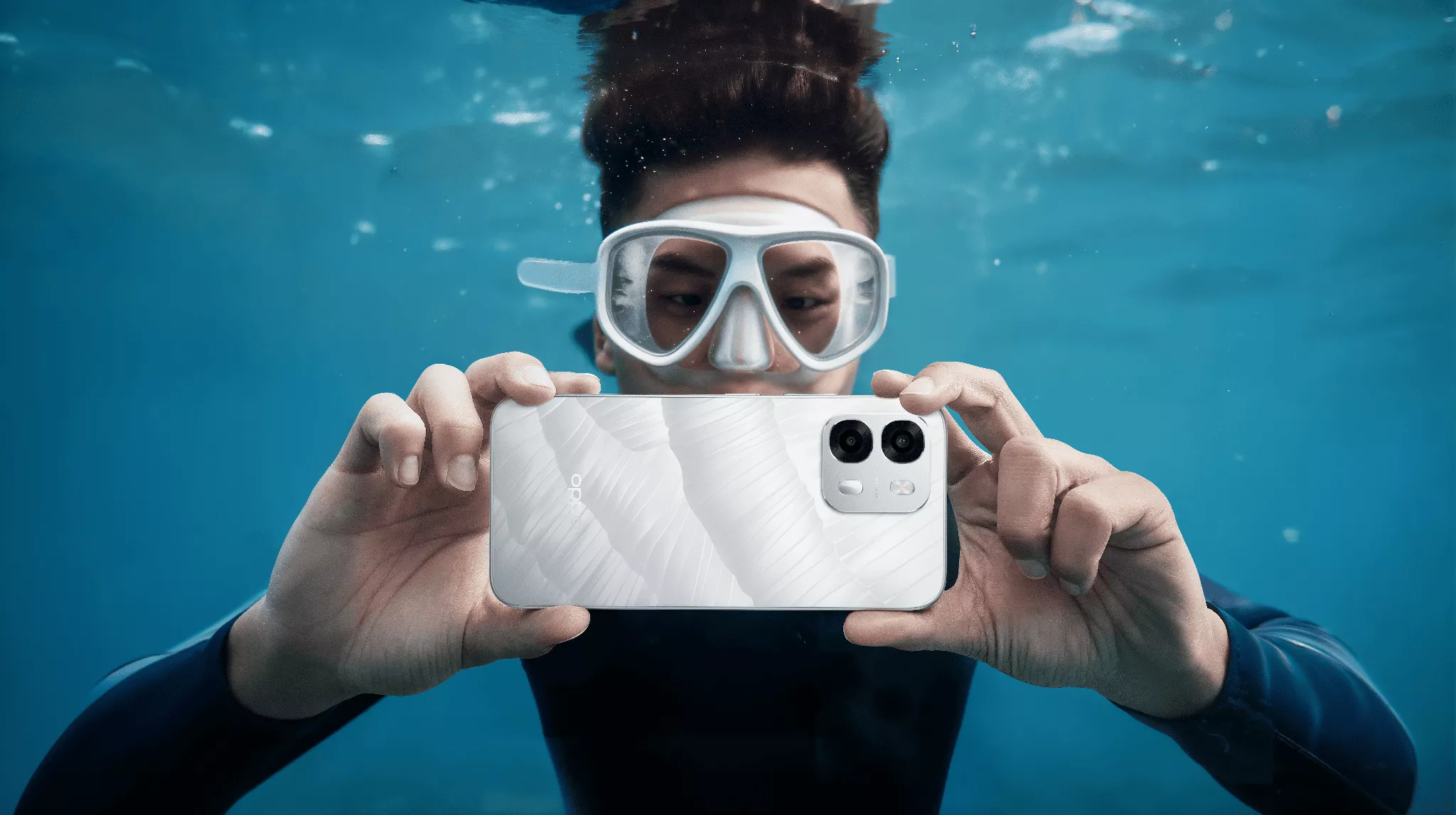 Seorang pria menggunakan kacamata renang memegang OPPO A6s untuk mengambil foto di dalam air, menunjukkan ketahanan rating IP69.