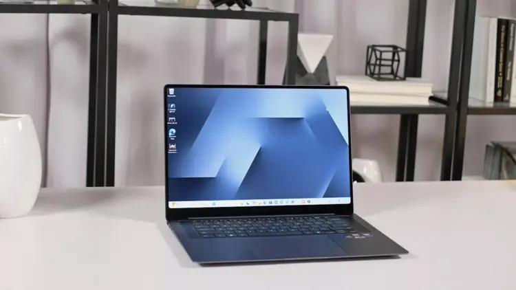 Tampilan layar AMOLED laptop Samsung Galaxy Book 6 dengan wallpaper biru minimalis di atas meja.