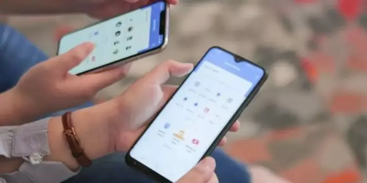 Dua orang sedang menggunakan smartphone mereka untuk memilih daftar penerima di aplikasi kirim THR online.