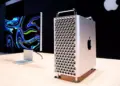 Mac Pro menara diletakkan di atas meja kayu di sebelah Pro Display XDR dengan latar belakang gelap, menunjukkan ekosistem kerja profesional Apple.