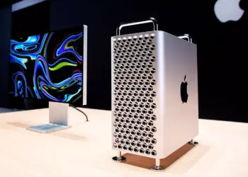 Mac Pro menara diletakkan di atas meja kayu di sebelah Pro Display XDR dengan latar belakang gelap, menunjukkan ekosistem kerja profesional Apple.