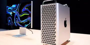 Mac Pro menara diletakkan di atas meja kayu di sebelah Pro Display XDR dengan latar belakang gelap, menunjukkan ekosistem kerja profesional Apple.
