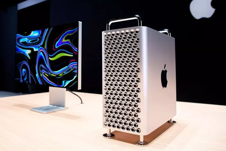 Mac Pro menara diletakkan di atas meja kayu di sebelah Pro Display XDR dengan latar belakang gelap, menunjukkan ekosistem kerja profesional Apple.