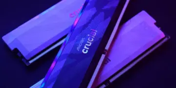Tiga keping RAM DDR5 merk Crucial dengan pencahayaan neon ungu kebiruan.
