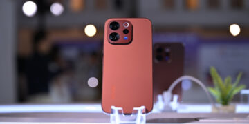 Smartphone Vivo V70 warna merah dengan modul kamera premium berdiri di display meja modern