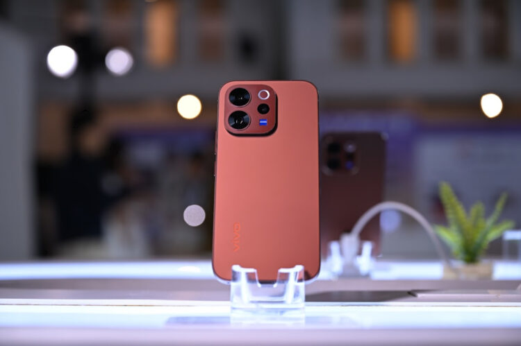 Smartphone Vivo V70 warna merah dengan modul kamera premium berdiri di display meja modern