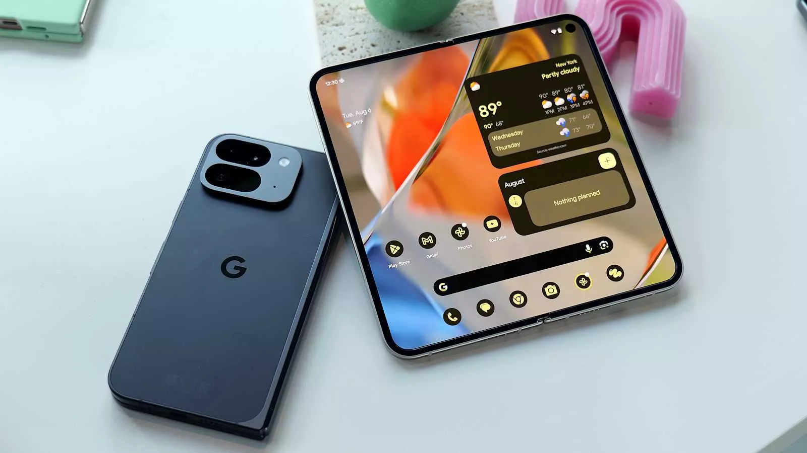 Google Pixel 9 Pro Fold posisi terbuka menampilkan layar internal lebar dengan widget AI Gemini Nano dan satu unit posisi tertutup warna hitam di sampingnya.