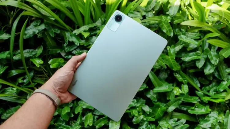Seseorang memegang tablet Xiaomi Redmi Pad 2 SE dengan latar belakang daun yang segar.