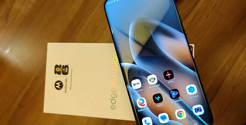 Penampakan unit smartphone Motorola Edge 70 Fusion dengan layar melengkung bersanding di samping kotak kemasannya.