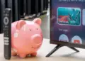 Ilustrasi celengan babi dan remote TV sebagai simbol harga Smart TV murah 2026 yang hemat biaya.