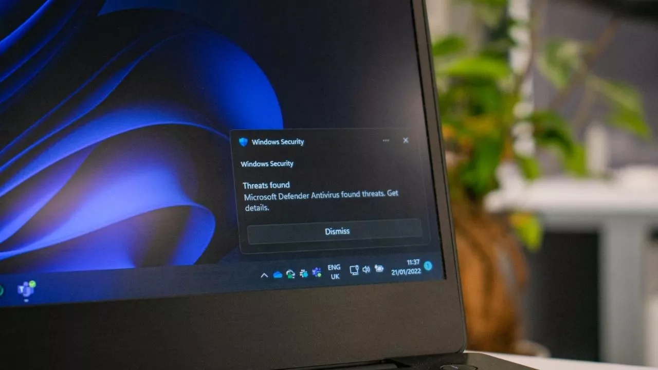 Notifikasi pop-up Windows Security berwarna gelap di pojok kanan bawah layar laptop, bertuliskan 'Threats found' dan 'Microsoft Defender Antivirus found threats'.