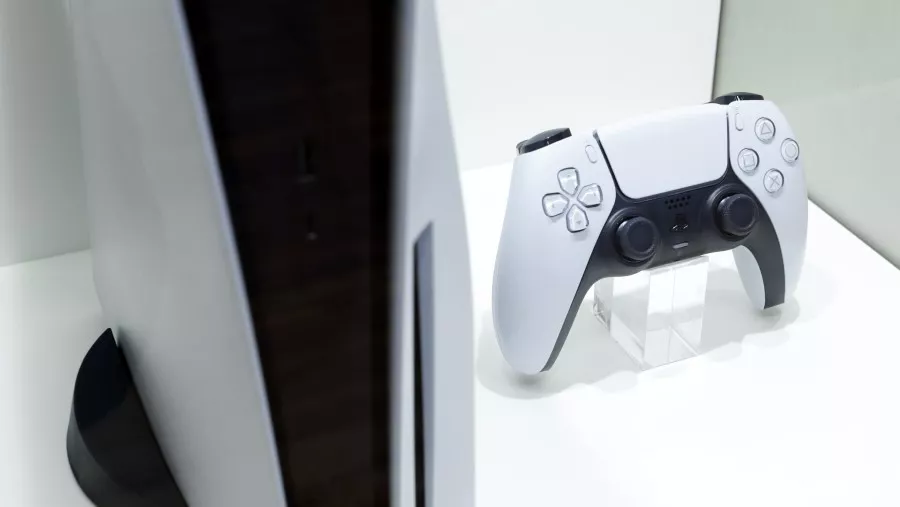 Close up controller DualSense PS5 yang dipajang di atas stand bening di samping konsol.