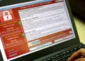 Layar laptop menampilkan serangan ransomware WannaCry dengan teks 'Ooops, your files have been encrypted!' dan permintaan tebusan Bitcoin.