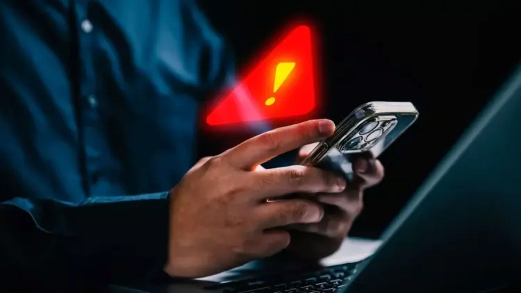 Seseorang memegang smartphone di depan laptop dengan simbol peringatan segitiga merah bercahaya dan tanda seru kuning besar yang melayang di atasnya, melambangkan peringatan infeksi Spyware Morpheus.