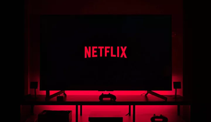Logo Netflix di layar televisi dalam ruangan gelap dengan pencahayaan merah di belakangnya.