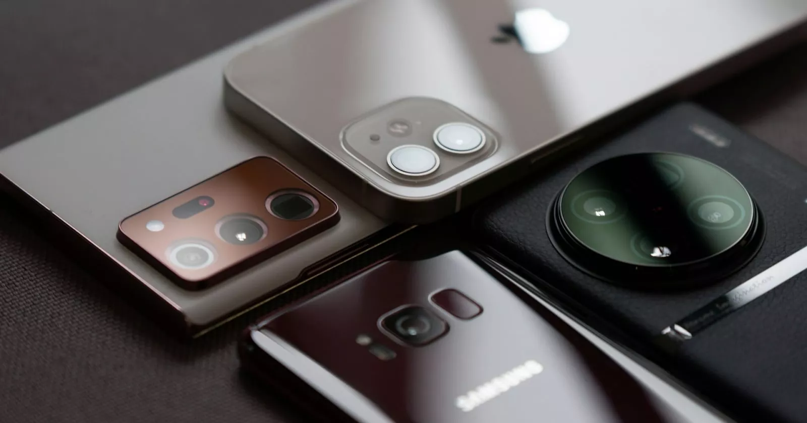 Tampilan jarak dekat berbagai modul kamera smartphone flagship, termasuk kamera Samsung Galaxy dan Apple iPhone yang diletakkan berdampingan secara estetik. Melambangkan persaingan sengit pangsa pasar smartphone global.