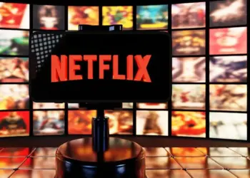 Smartphone menampilkan logo Netflix di depan latar belakang banyak poster film dan serial original.