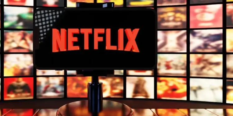 Smartphone menampilkan logo Netflix di depan latar belakang banyak poster film dan serial original.