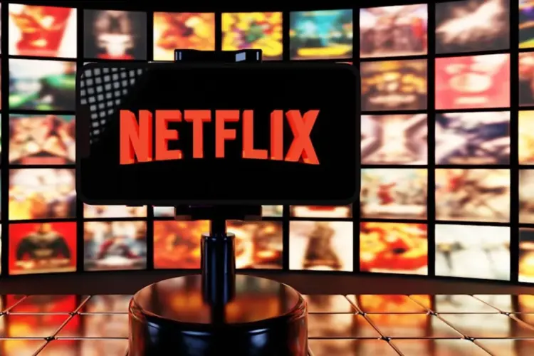 Smartphone menampilkan logo Netflix di depan latar belakang banyak poster film dan serial original.