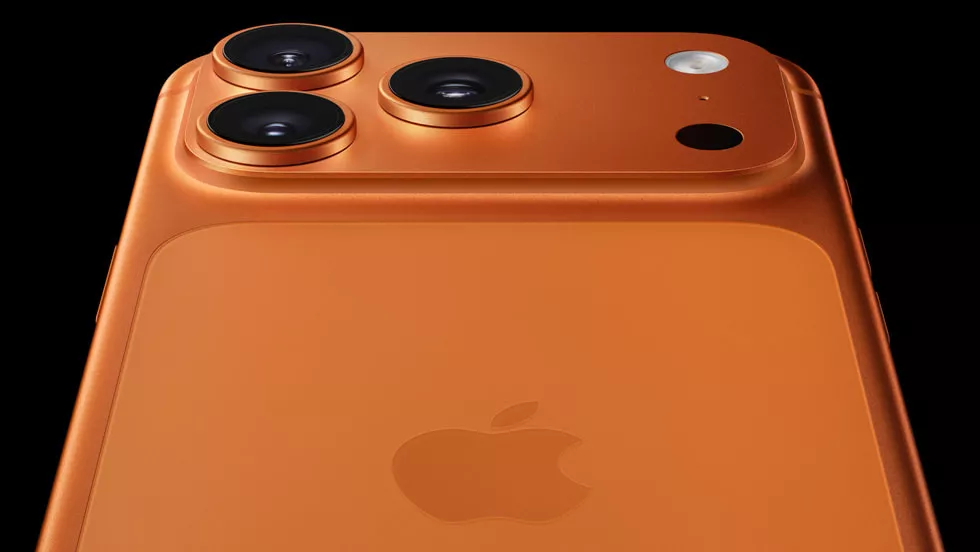 Tampilan bodi belakang iPhone dengan warna oranye titanium yang mencolok, memperlihatkan logo Apple dan tiga lensa kamera besar. Visual untuk menganalisis posisi Apple yang tergeser oleh Samsung.
