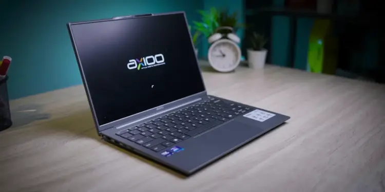 Laptop Axioo Hype AI 5 berwarna abu-abu terbuka di atas meja kayu di studio meja kerja.