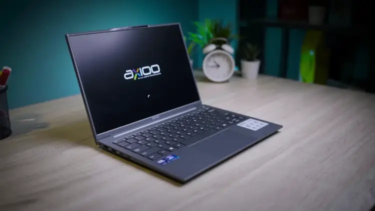 Laptop Axioo Hype AI 5 berwarna abu-abu terbuka di atas meja kayu di studio meja kerja.