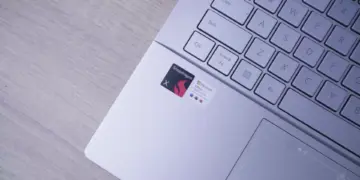 Close-up area palm rest Laptop AI ASUS Vivobook S14 menampilkan stiker 'Powered by Snapdragon X' dan 'Microsoft Office'.