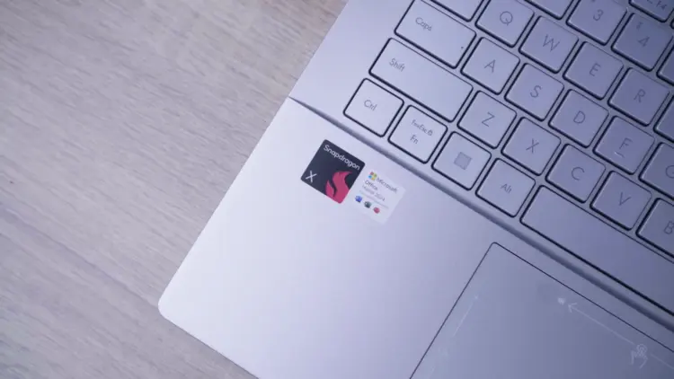 Close-up area palm rest Laptop AI ASUS Vivobook S14 menampilkan stiker 'Powered by Snapdragon X' dan 'Microsoft Office'.