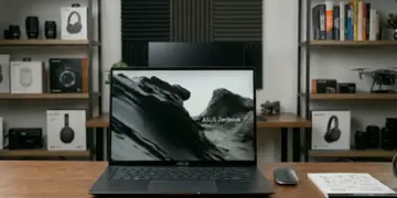 Laptop ASUS Zenbook S16 OLED UM5606GA di atas meja kerja dengan layar menampilkan wallpaper pegunungan