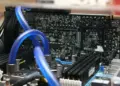 Detail sirkuit komponen motherboard PC dengan sistem pendingin air (liquid cooling) berwarna biru yang menunjukkan kompleksitas rakitan komputer modern.