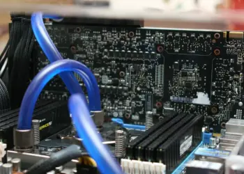 Detail sirkuit komponen motherboard PC dengan sistem pendingin air (liquid cooling) berwarna biru yang menunjukkan kompleksitas rakitan komputer modern.