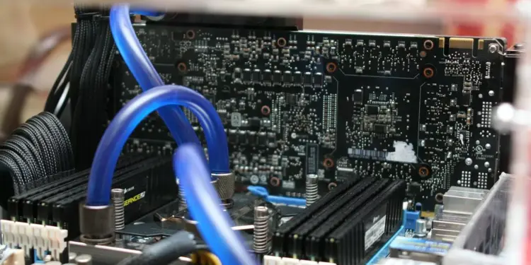 Detail sirkuit komponen motherboard PC dengan sistem pendingin air (liquid cooling) berwarna biru yang menunjukkan kompleksitas rakitan komputer modern.