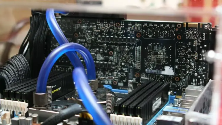 Detail sirkuit komponen motherboard PC dengan sistem pendingin air (liquid cooling) berwarna biru yang menunjukkan kompleksitas rakitan komputer modern.
