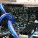 Detail sirkuit komponen motherboard PC dengan sistem pendingin air (liquid cooling) berwarna biru yang menunjukkan kompleksitas rakitan komputer modern.