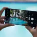 Seseorang memegang smartphone Samsung dengan layar penuh sedang membidik pemandangan kolam renang menggunakan fitur pengunci fokus kamera