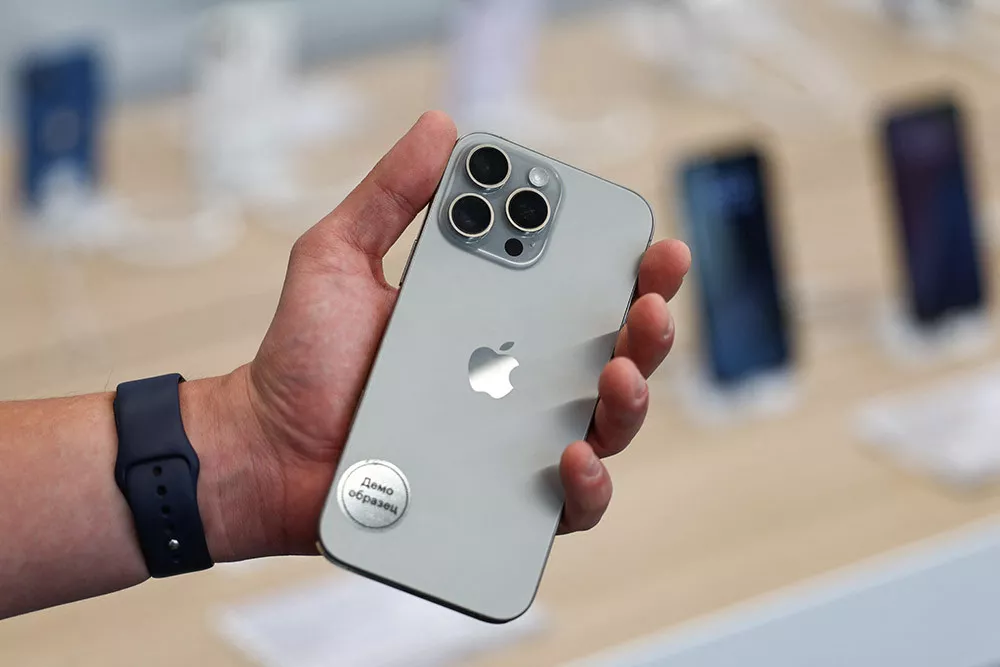Tampilan bodi belakang iPhone varian Pro berwarna titanium yang digenggam dengan satu tangan di sebuah toko ritel.
