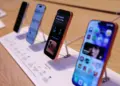 Jajaran unit demo iPhone terbaru yang dipajang di atas meja kayu menggunakan penyangga display khusus toko resmi Apple.