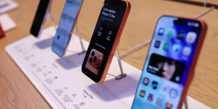Jajaran unit demo iPhone terbaru yang dipajang di atas meja kayu menggunakan penyangga display khusus toko resmi Apple.