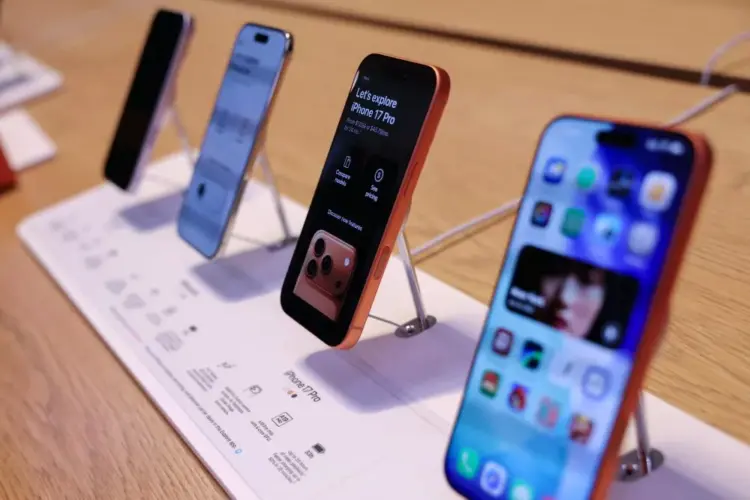 Jajaran unit demo iPhone terbaru yang dipajang di atas meja kayu menggunakan penyangga display khusus toko resmi Apple.