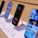 Jajaran unit demo iPhone terbaru yang dipajang di atas meja kayu menggunakan penyangga display khusus toko resmi Apple.