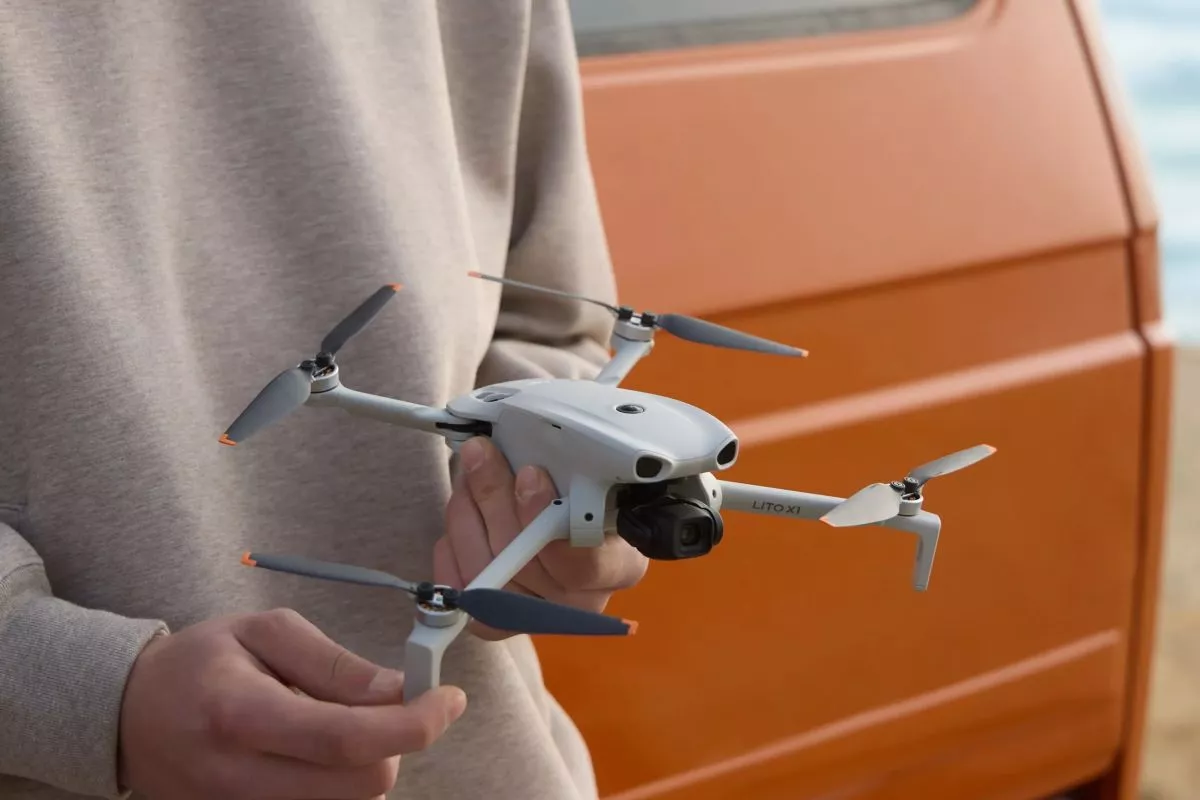 Seseorang sedang memegang unit drone DJI Lito X1 berwarna abu-abu dengan desain ringkas dan baling-baling lipat.