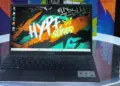 Laptop Axioo Hype Series varian Intel Core i3 dengan wallpaper bertuliskan Hype Series diletakkan di atas meja kaca.